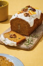 A freshly baked carrot cake loaf adorned with smooth cream cheese frosting, walnut pieces, and