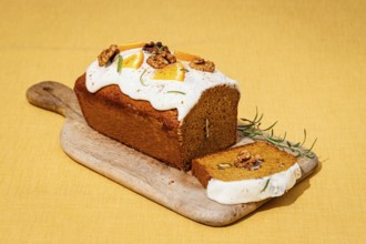 A freshly baked carrot cake loaf topped with cream cheese frosting, garnished with walnuts and