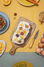 Carrot cake loaf topped with cream cheese frosting, orange slices, walnut, and rosemary Set on a