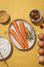 A vibrant assembly of fresh carrots, eggs, walnuts, and rosemary on a yellow linen backdrop,