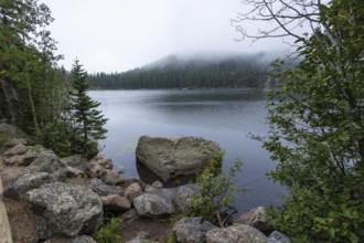 A serene view of a calm lake surrounded by lush greenery and rocky terrain under a blanket of