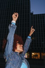 A joyful African descendant woman with afro hair raises her arms in celebration against a backdrop