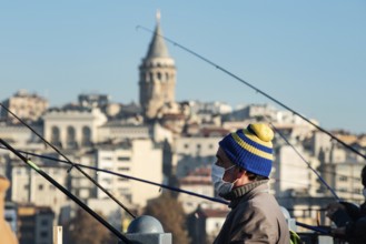 Istanbul, Turkey. November 28th 2020 A man wearing a facemask fishing from the Galata Bridge in