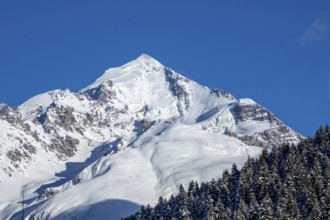 A stunning snow-covered mountain peak stands majestically against a backdrop of a clear, deep blue