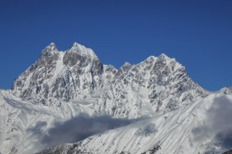 Majestic snow-covered mountain peaks tower under a clear blue sky, creating a breathtaking natural