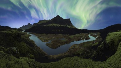 The Northern Lights unfurl in a vibrant dance across the night sky over Iceland's rugged terrain,