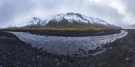 A dramatic view of a snow-covered mountain rising over a rocky riverbed in the Icelandic Highlands,