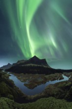 Vivid green Northern Lights dance in the sky above the dark silhouette of Iceland's rugged mountain
