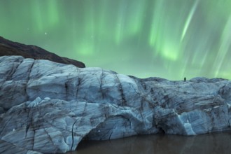 A solitary figure stands atop a glacier in Iceland, gazing at the mesmerizing Northern Lights that
