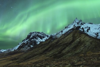 A mesmerizing northern light display dances above snow-capped mountains under a starry Icelandic