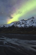Captivating Northern Lights (Aurora Borealis) shine above snow-covered peaks and a riverbed in the