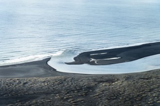 Aerial view of a winding Icelandic river meeting the sea. Black sand contrasts with the blue water,