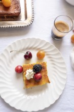 Top view of a gourmet desert scene on a light tablecloth, featuring a piece of cake topped with