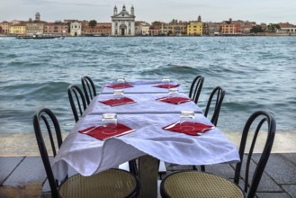 Restaurant tables on the shore in windy weather, on the island of Giudecca, Venice behind, Veneto,