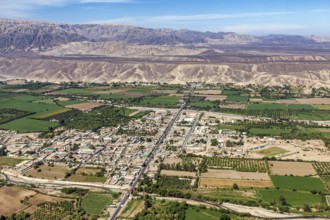 Expansive aerial view of a city with green fields and mountains in the background, The city of