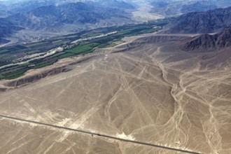 View of Nazca lines with contrasting green fields and mountain ranges in the background, the