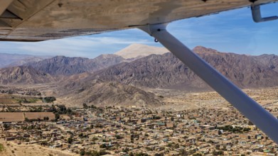 Aerial view of a city surrounded by mountains, viewed from the window of an airplane in clear