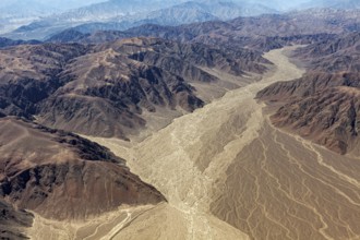 Aerial view of a dry mountain landscape with a dried-out riverbed surrounded by brown and