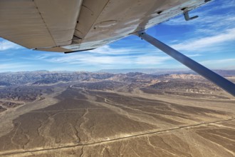 View from an airplane over desert and mountains under a blue sky, the desert landscape near Nasca