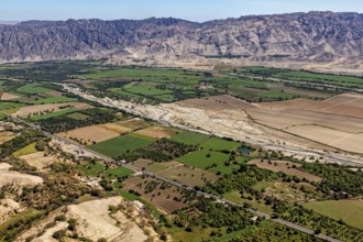 Green fields and river valley in front of a rocky mountain range under clear sky, the desert