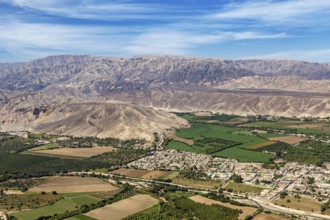 Diverse landscape with green fields and cityscape in front of a mountain panorama, The desert