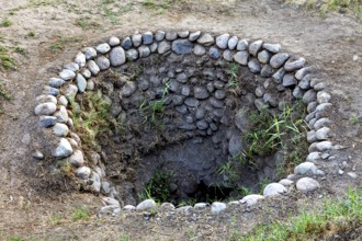 Circular hole in the ground with a rim of stones and some vegetation, The ancient Nazca wells