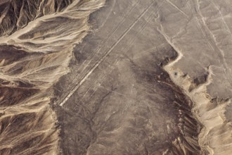 Sand-colored desert landscape with visible geoglyphs and linear patterns, surrounded by mountains,