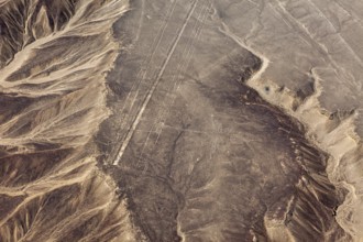 Aerial view of lines and geoglyphs in a sandy desert landscape with adjacent mountains, the