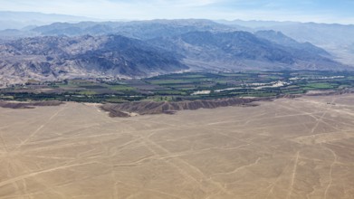 An aerial view of a desert landscape with a green oasis and mountains in the background, The