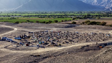 Rural cemetery in dry surroundings with green fields and mountain scenery in the background,
