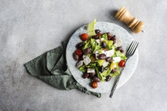 A vibrant Greek salad featuring tomatoes, lettuce, red fermented olives, and feta cheese, drizzled