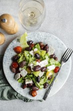 A vibrant Greek salad featuring fresh tomatoes, crisp lettuce, red fermented olives, and creamy