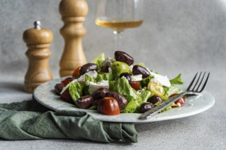 A vibrant Greek salad featuring tomatoes, lettuce, red olives, feta cheese, and olive oil A glass
