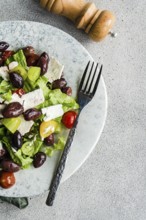 A vibrant Greek salad with tomatoes, lettuce, red olives, and feta cheese Complemented by a pepper