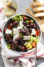 A bowl of Greek salad with tomatoes, lettuce, red fermented olives, oil, and feta cheese