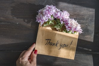 A hand holds a brown envelope with Thank you written on it, containing delicate pink chrysanthemums