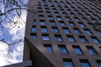 A low angle shot of a tall modern skyscraper set against a blue sky, featuring rows of windows and