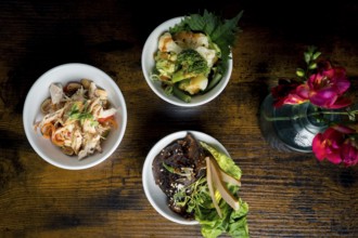 Top-down view of three gourmet bowls, broccoli and cauliflower in satay sauce, chicken with glass