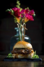 A gourmet pulled pork slider presented elegantly with colorful flowers in the background The food