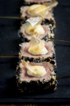 Close-up of rare tuna steaks coated in sesame seeds, topped with mayonnaise and garnished with