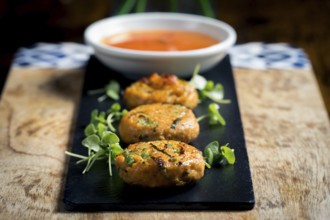Close-up of golden corn and spring onion patties served with fresh greens and accompanied by a bowl