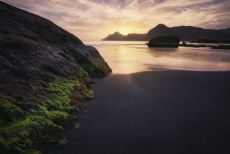 The tranquil sunset casts a golden hue over the rugged rocks and calm waters of Cala del Lastre in