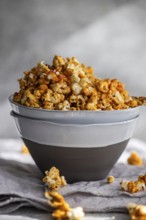 Grey bowl overflowing with sweet caramel popcorn on a textured grey cloth, showcasing a delicious