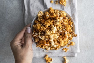 Cropped unrecognizable person holding a bowl of sweet caramel popcorn in a top view, displaying the