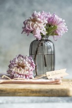 Elegant pink chrysanthemums in a ribbed glass vase on a wooden surface with a tag reading Autumn