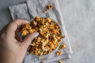 Cropped unrecognizable person's hand picking sweet caramel popcorn from a gray bowl, set against a