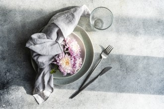 An elegant table setting featuring pink chrysanthemums on a grey plate, accompanied by a linen