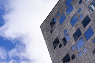From below view of a corner of a modern textured building facade featuring multiple aligned blue