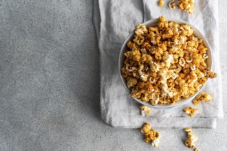 Top view of a bowl full of sweet caramel popcorn, sprinkled with sugar and spices, on a textured