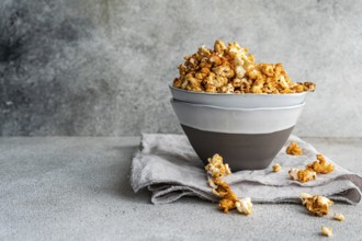 Gray bowl overflowing with sweet caramel popcorn is set on a textured linen, against a textured